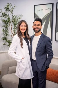  Dr. Pinky Vanmali in white lab coat standing with male professional in dark suit, both smiling in modern medical office waiting area with contemporary decor and artwork Copy Ask Qwen Explain Translate(en-US)